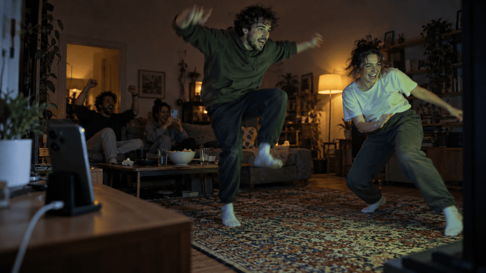 Two friends jumping and dodging in front of a TV while a phone on a stand tracks their movement
