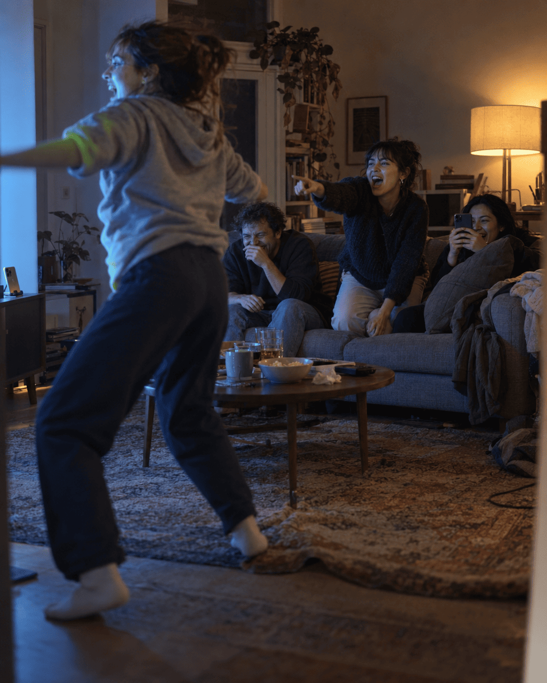 Friends laughing on the couch while one player jumps during a game